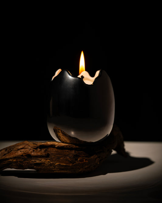 Lit candle glowing warmly inside silver egg-shaped Ovonique jar in a dark setting